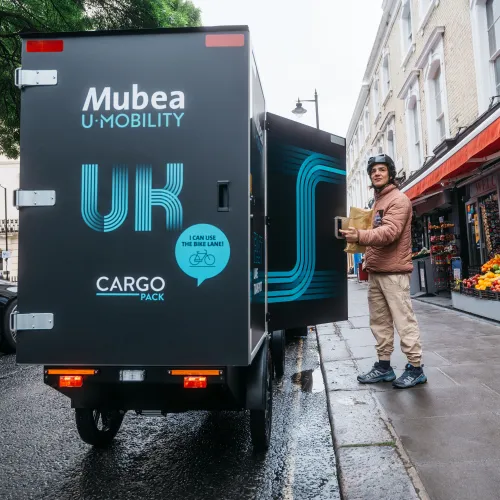 Delivery driver unloading goods from an electric cargo vehicle outside a neighborhood market