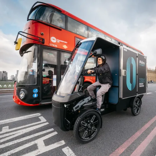 Electric cargo vehicle drives across Westminster Bridge beside a London double-decker bus.