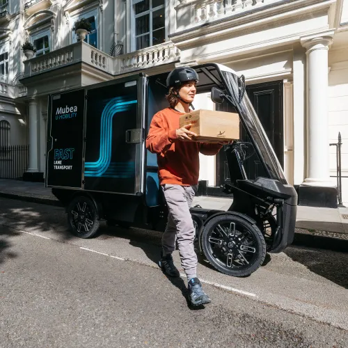 Delivery worker unloads a package from an electric cargo vehicle on a residential city street.
