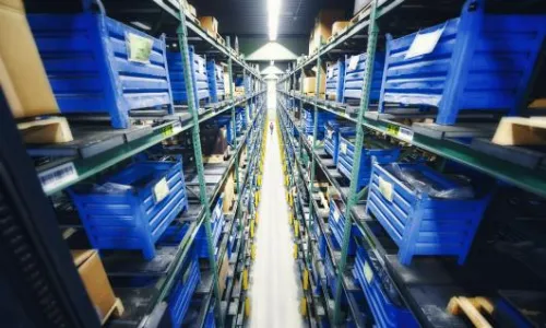 Shelf racks with blue storage bins containing spare parts in a long warehouse aisle