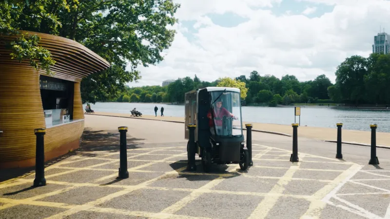 Electric cargo vehicle drives along a lakeside path in a green urban park.