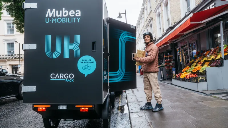 Delivery driver unloading goods from an electric cargo vehicle outside a neighborhood market