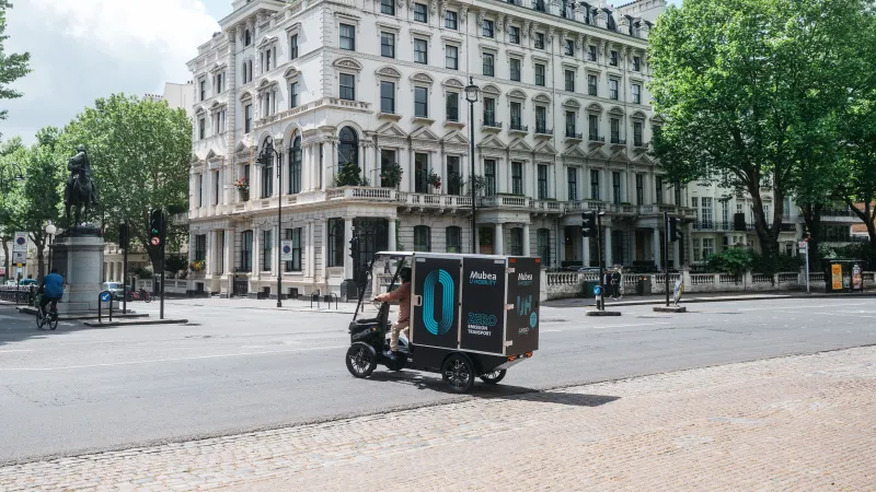Electric cargo vehicle crosses a city square in front of a historic building.